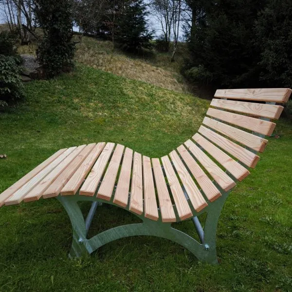 Seitenansicht einer Ergonomischen Wellenliege / Waldsofa aus Douglasienholz mit feuerverzinktem Stahluntergestell auf einer Grünfläche.